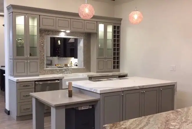 Gray shaker cabinets with glass-front uppers, a built-in wine rack and a white stone island under pink glass pendants