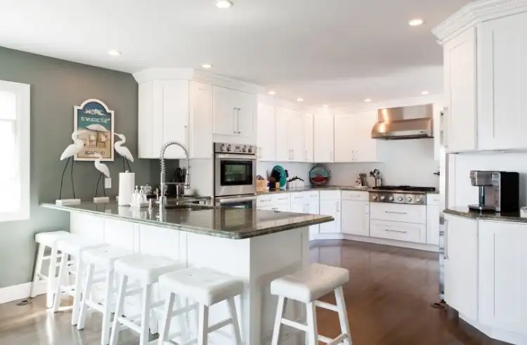 White shaker kitchen cabinets with a dark granite peninsula, white bar stools and a stainless range hood, kitchen cabinets Tennessee